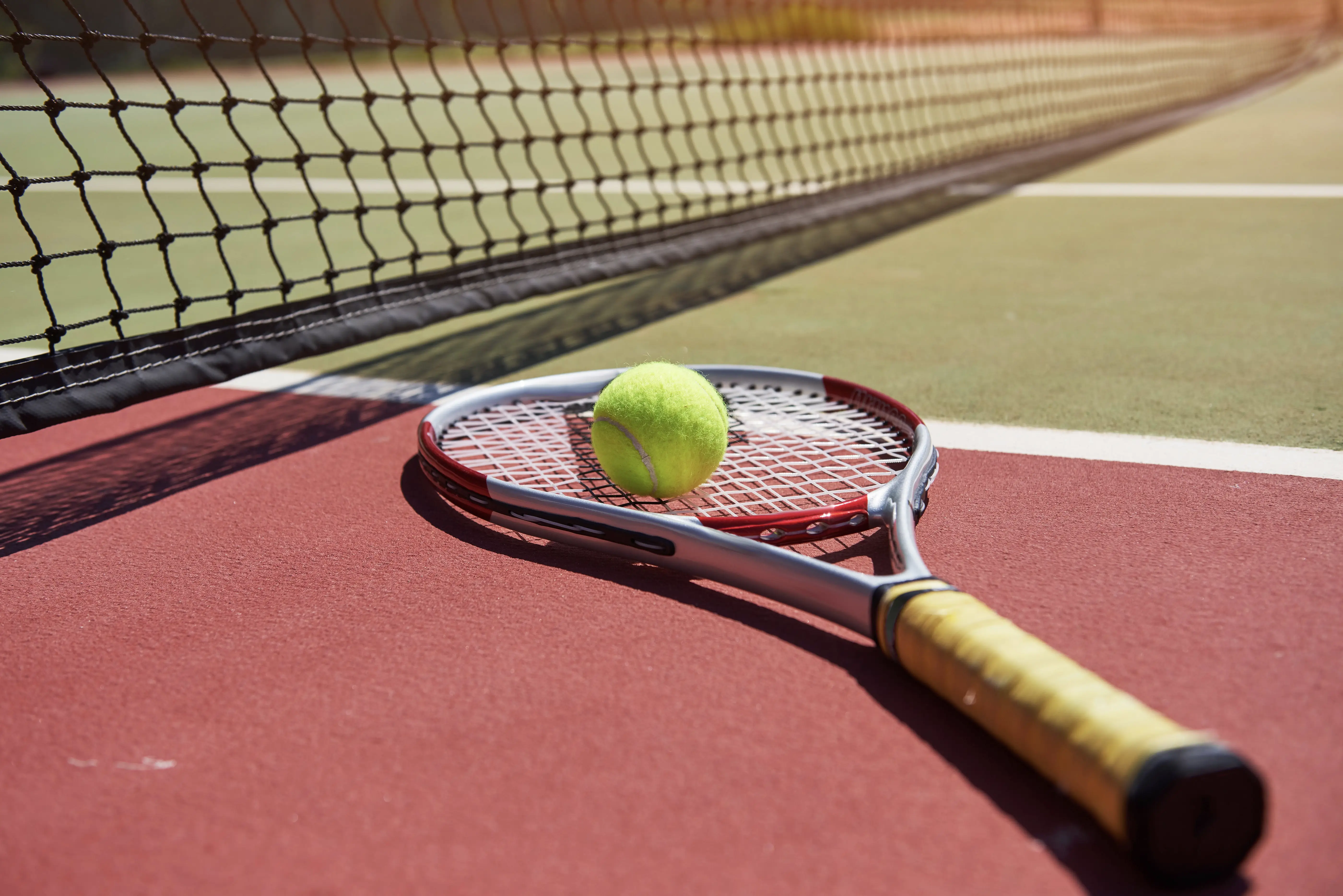 Uma raquete de tênis e bola de tênis nova em uma quadra de tênis recém pintada.